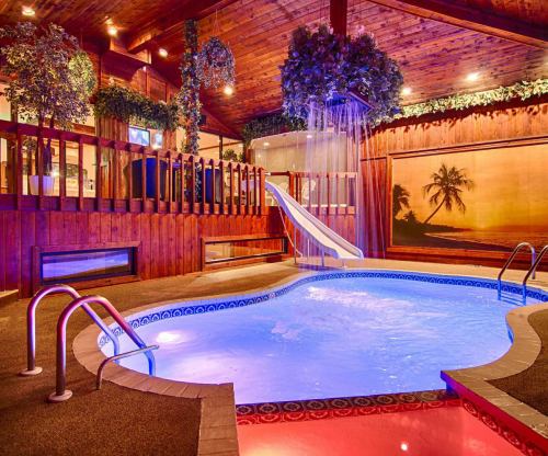 Indoor pool area with a slide, surrounded by wooden decor and tropical-themed artwork, illuminated with warm lighting.