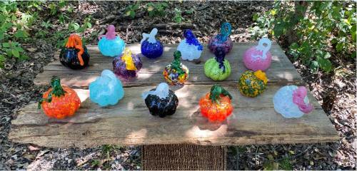 A wooden table in a forest displays colorful, decorative pumpkins in various shapes and sizes.