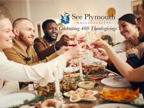 A diverse group of friends toasting with drinks at a festive Thanksgiving dinner table filled with food.
