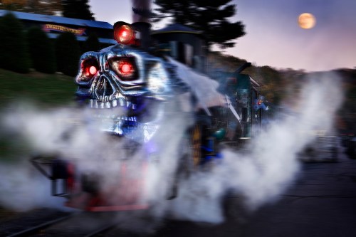 A spooky train with glowing red eyes and a skull design emits steam under a full moon.