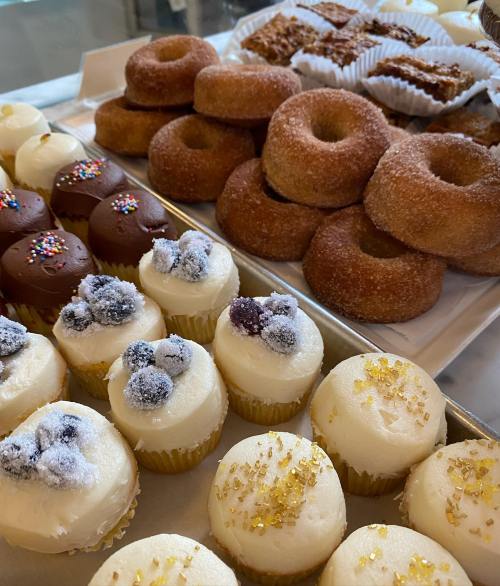 A variety of desserts including cupcakes with frosting, donuts, and pastries arranged on trays.
