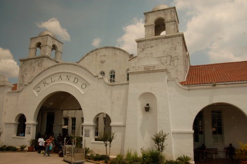 Historic white building with arched entrance, featuring the name "Orlando" and surrounded by greenery and people.