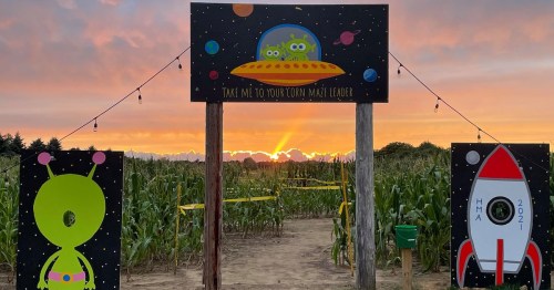 A colorful alien-themed entrance to a corn maze at sunset, featuring a spaceship and rocket illustrations.