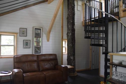 Cozy interior of a cabin featuring a leather sofa, spiral staircase, and a tree integrated into the design.