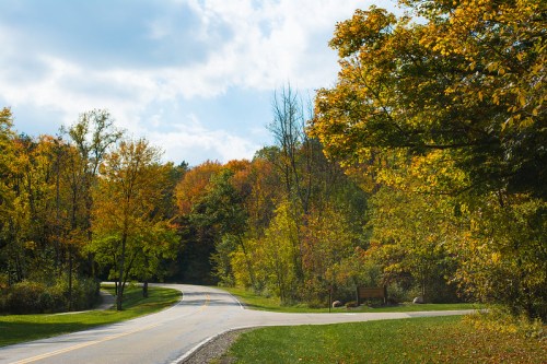 A winding road surrounded by colorful autumn trees under a partly cloudy sky.