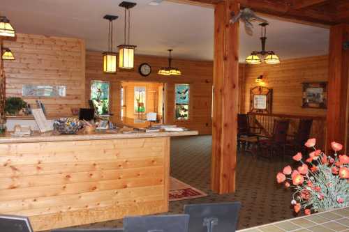 Cozy wooden reception area with a front desk, warm lighting, and decorative elements, including flowers and artwork.