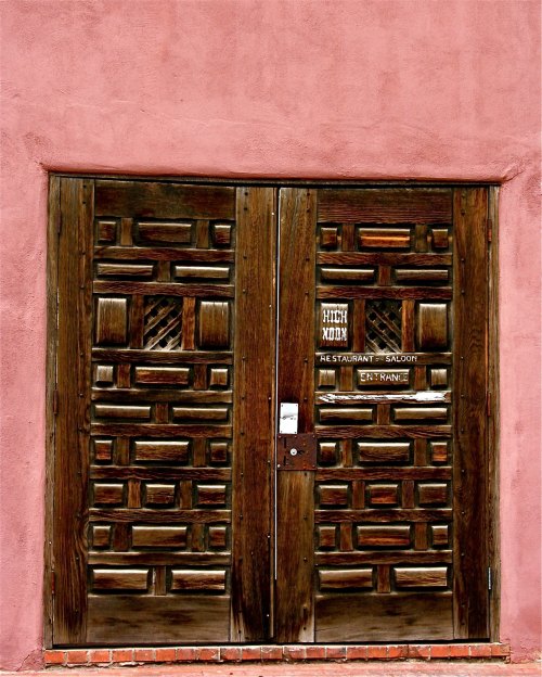 A rustic wooden door with intricate carvings, featuring a sign that reads "High Noon Restaurant Saloon."