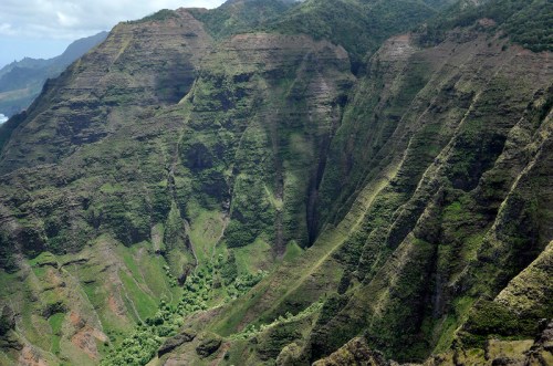 Lush green mountains with steep, rugged slopes and deep valleys under a clear sky.