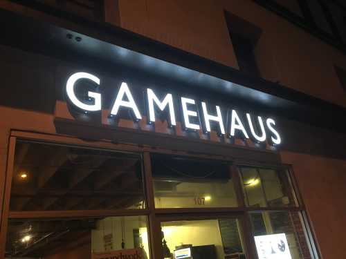 Illuminated sign for "GAMEHAUS" on a building at night, with a window visible below.