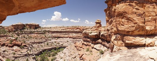A panoramic view of rugged rock formations and a winding river in a canyon under a clear blue sky.