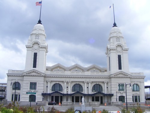 Historic white train station with two tall towers, American flag flying, under a cloudy sky.