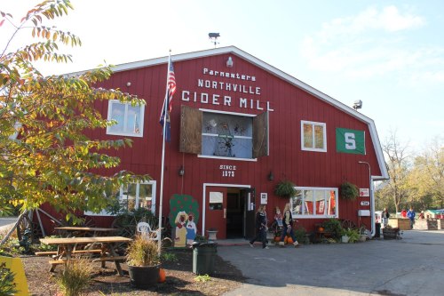 Red barn-style building with "Northville Cider Mill" sign, American flag, and seasonal decorations outside.