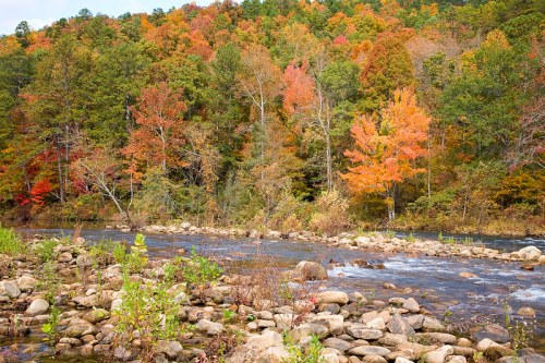 A serene river flows through a landscape of colorful autumn trees and rocky banks, showcasing vibrant fall foliage.