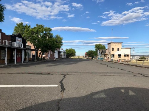 A quiet, empty street lined with old buildings under a blue sky with scattered clouds.