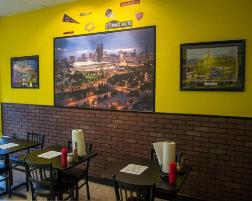 Interior of a restaurant featuring yellow walls, framed cityscape photos, and tables with condiments.