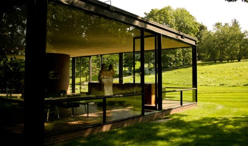 A modern glass house surrounded by lush greenery, with two people inside enjoying the serene view.
