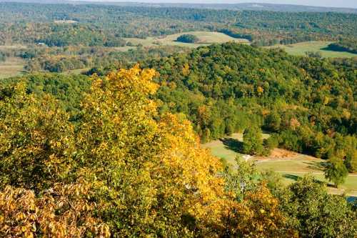 A scenic view of rolling hills and trees in autumn colors, with a golf course visible in the foreground.