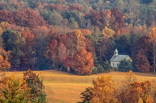 A quaint church nestled among vibrant autumn trees in a colorful landscape.