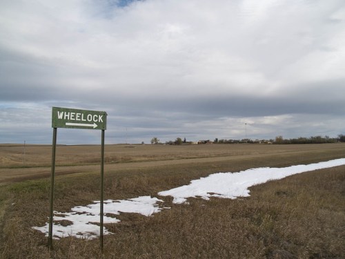 Signpost for Wheelock beside a snowy patch in a rural landscape under a cloudy sky.