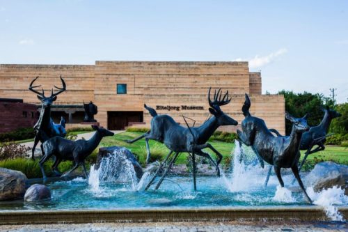 A bronze sculpture of deer leaping through water in front of the Bison Museum, with a modern building in the background.