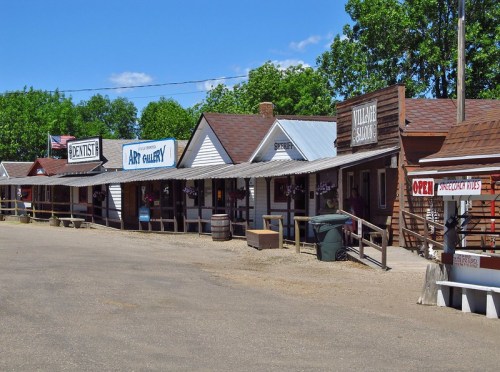A row of old-fashioned storefronts in a western-style town, featuring signs for a dentist, art gallery, and saloon.