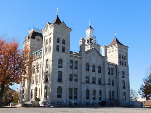 Historic stone building with ornate architecture, featuring towers and a clock, set against a clear blue sky.