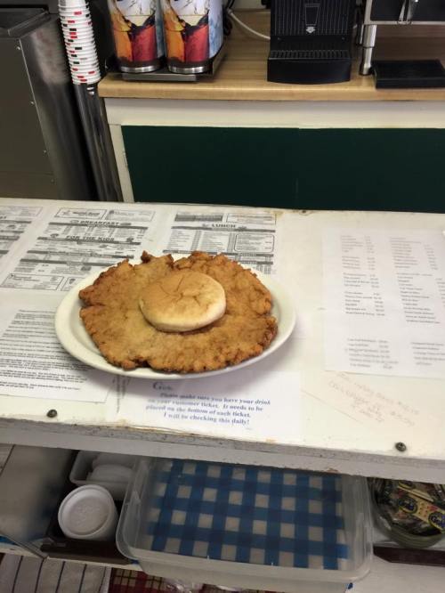 A large, crispy fried dish with a small bun on top, placed on a white plate on a counter.