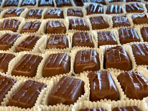 A close-up of neatly arranged chocolate-covered candies in white paper cups.