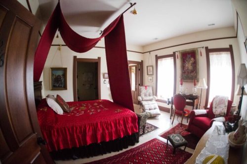 Cozy bedroom featuring a red canopy bed, elegant furnishings, and warm lighting, creating a welcoming atmosphere.