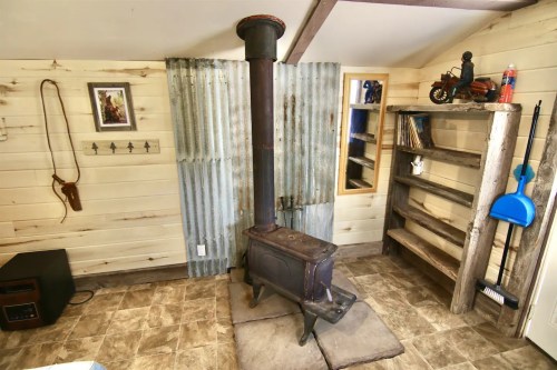 A rustic room featuring a wood stove, metal wall, shelves with books, and a few decorative items.