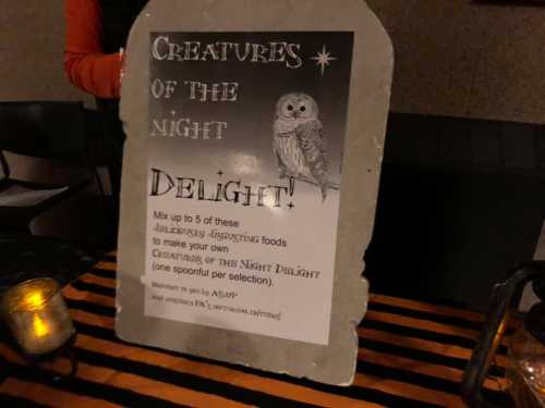 A sign reading "Creatures of the Night Delight!" with an owl graphic, inviting guests to mix spooky foods.