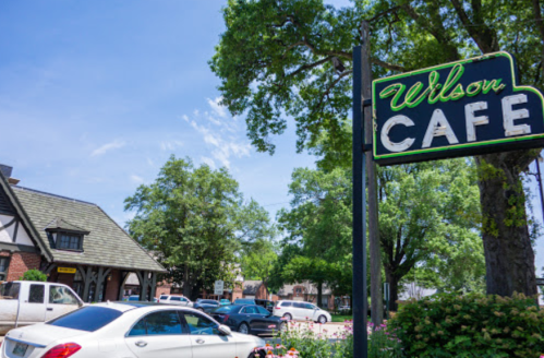 A sunny day view of Wilson Cafe sign with trees and parked cars in the background.