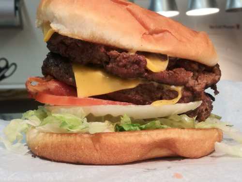 A towering burger with two beef patties, melted cheese, lettuce, tomato, and onion, all in a toasted bun.