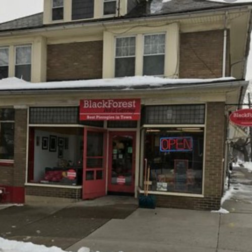 A storefront of "BlackForest" with a sign reading "Best Pierogies in Town" and an "OPEN" neon sign, surrounded by snow.