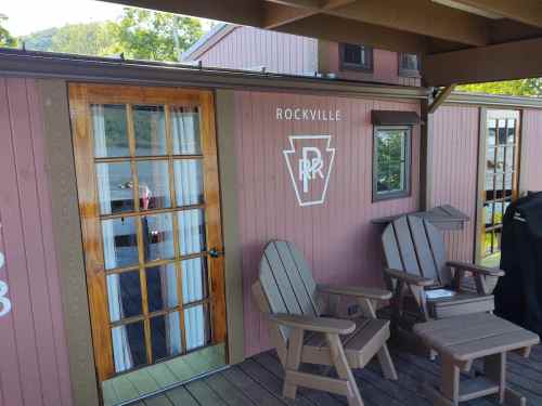 A wooden deck with two chairs in front of a pink building featuring a glass door and a logo that reads "Rockville."