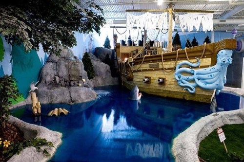 A whimsical indoor scene featuring a pirate ship, an octopus, and a blue water area surrounded by rocks and trees.