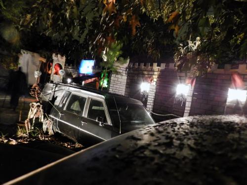 A spooky scene featuring a hearse in front of a castle-like structure, decorated with skeletons and eerie lighting.