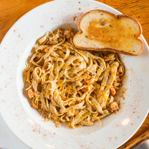A plate of creamy pasta with shrimp, topped with cheese, served with a slice of toasted bread on the side.