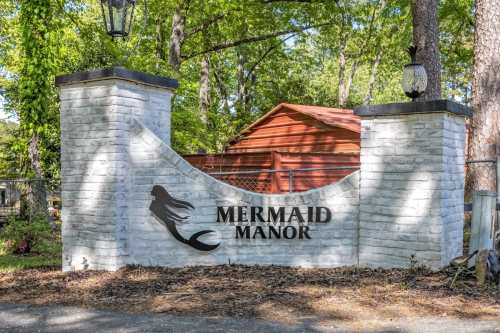 Sign for "Mermaid Manor" at a property entrance, featuring a silhouette of a mermaid and surrounded by trees.