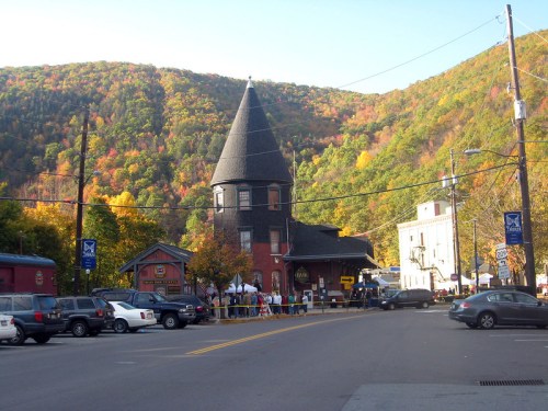A quaint town scene with a tall, black tower building surrounded by colorful autumn foliage and parked cars.