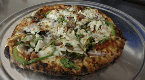A freshly baked pizza topped with cheese, vegetables, and herbs on a metal tray.