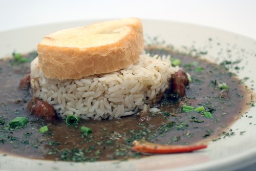 A plate of rice topped with a slice of bread, surrounded by a dark sauce and garnished with herbs and green onions.