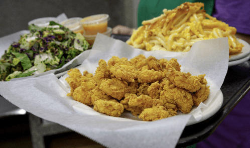 A plate of golden fried chicken tenders with a side of salad and macaroni and cheese in the background.