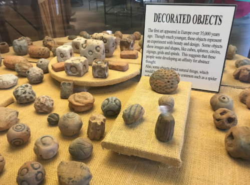 A display of ancient decorated objects, including various shapes and designs, with an informational sign in the background.
