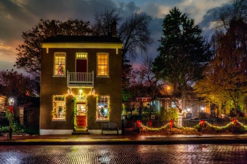 A charming two-story house adorned with festive lights and decorations, set against a twilight sky.