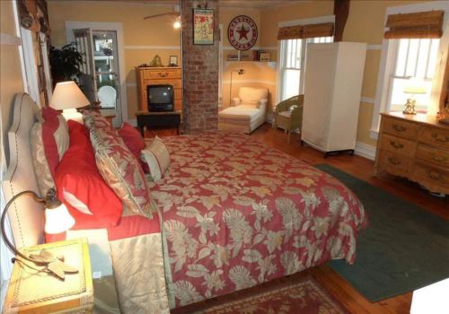 Cozy bedroom with a large bed, vintage decor, a TV, and a seating area, featuring warm colors and wooden accents.