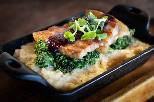 A sizzling dish featuring grilled fish on a bed of kale and creamy mashed potatoes, garnished with microgreens.