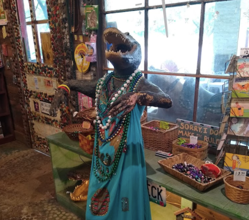 A colorful display featuring a crocodile statue adorned with beads and a blue dress in a quirky shop.
