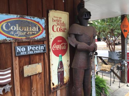 A rustic wooden wall features vintage signs and a metal knight statue beside a Coca-Cola advertisement.