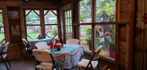 Cozy interior of a rustic dining area with tables, chairs, and large windows overlooking a garden.